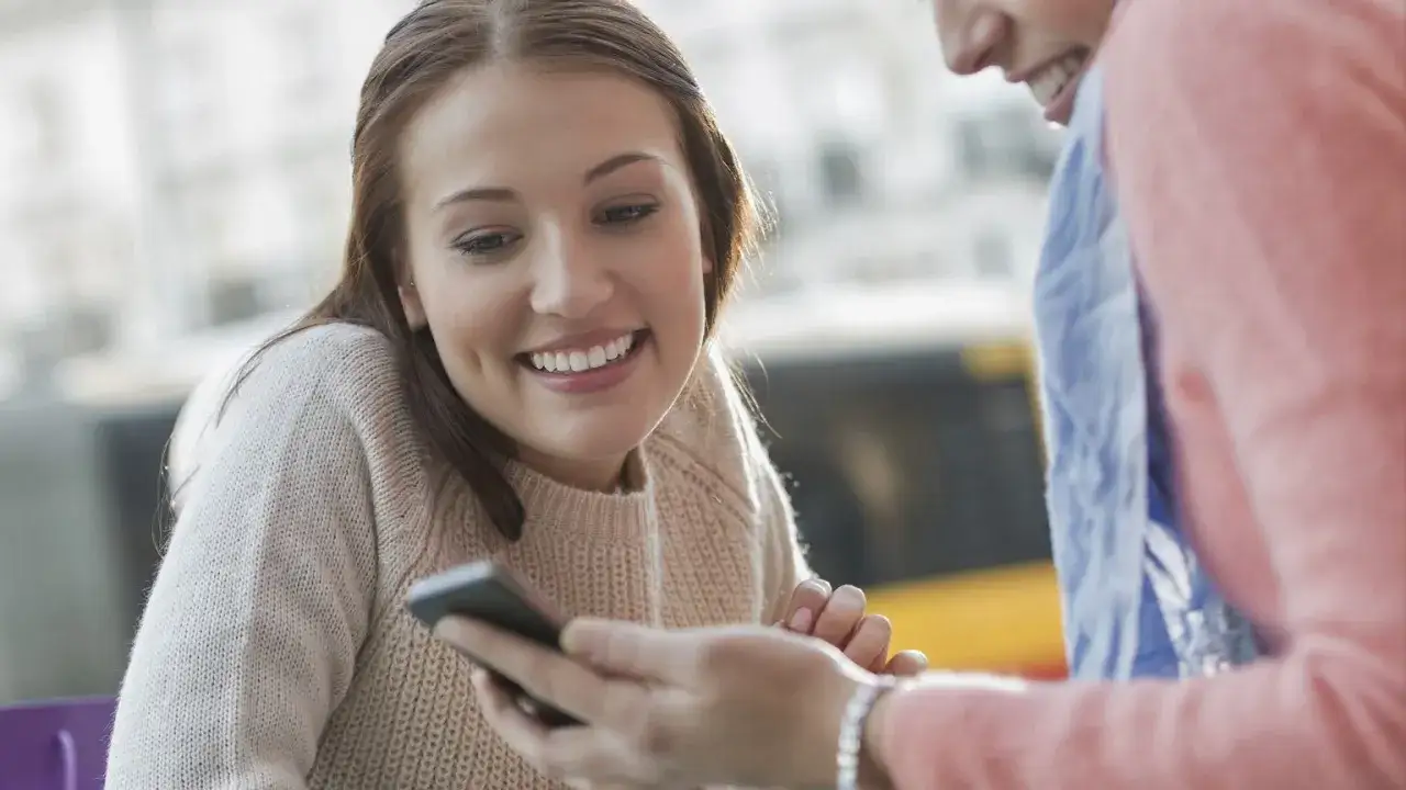 Uśmiechnięta dziewczyna czyta wiadomość, jak pisze zakochany facet. Jej oczy błyszczą, a dołeczki na policzkach dodają uroku.