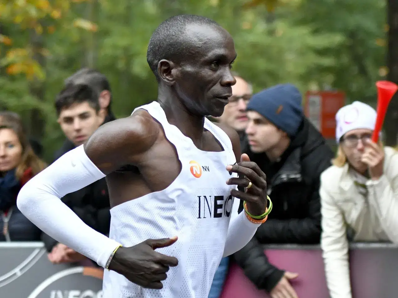 Eliud Kipchoge biegnie, ustanawiając nowy maraton rekord świata. Widzowie dopingują go zza barierek.