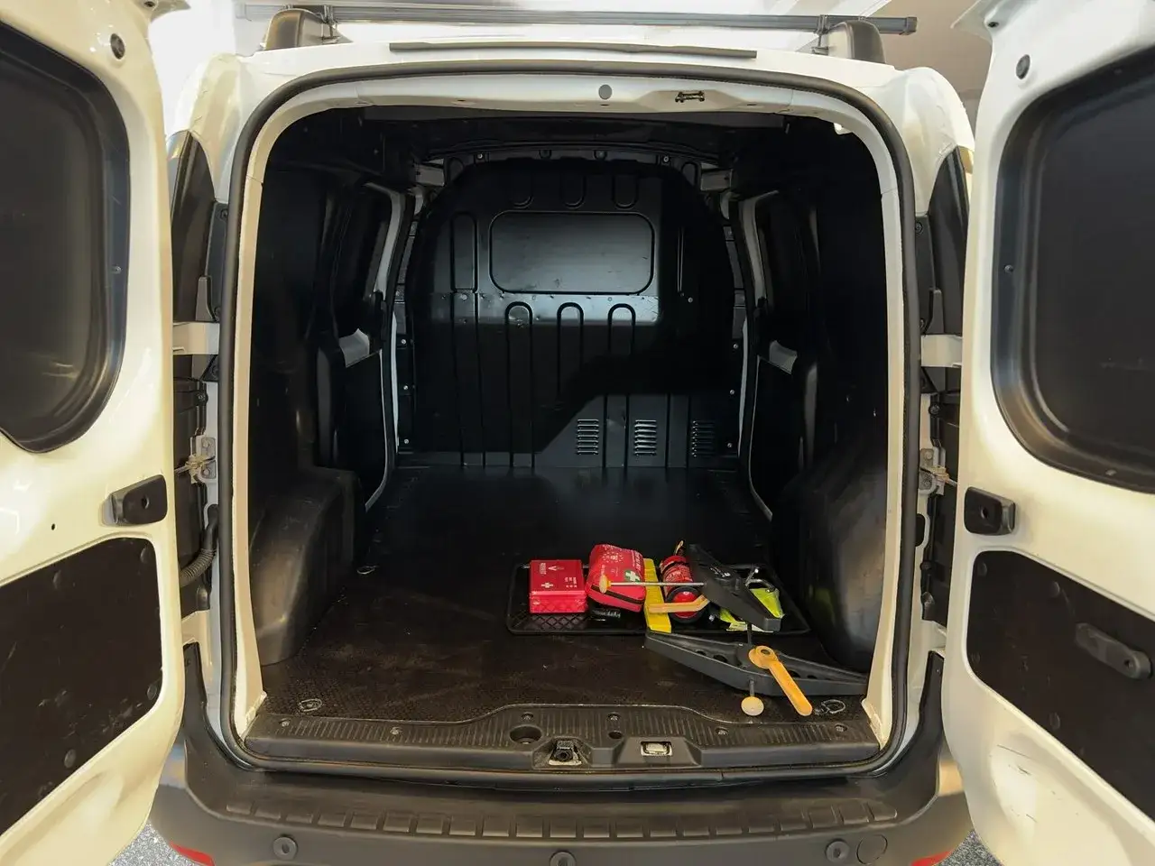 Pusta przestrzeń ładunkowa białego Dacia Dokker Stepway z otwartymi tylnymi drzwiami. Na podłodze leży apteczka i narzędzia.