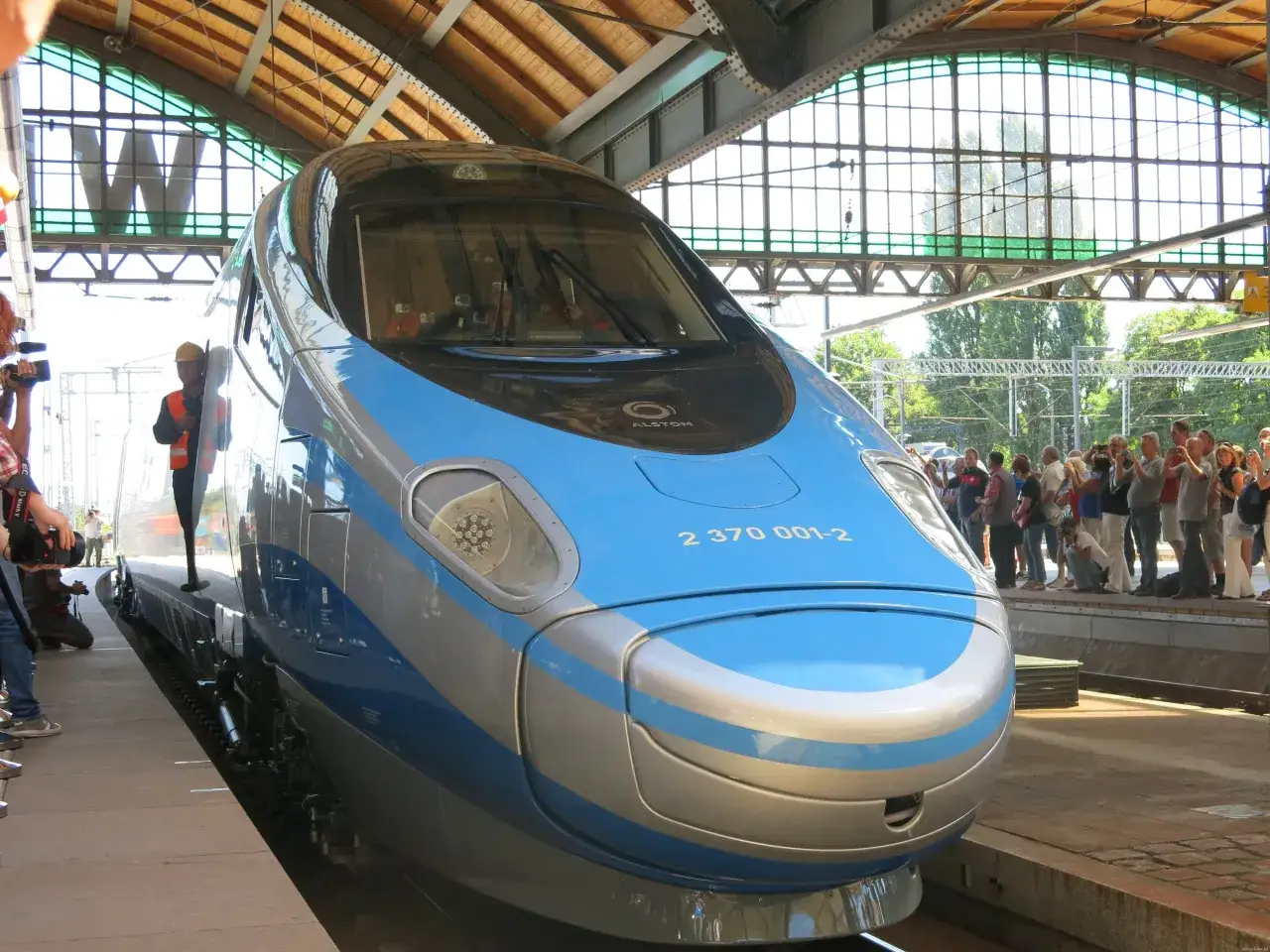 Nowoczesny pociąg Pendolino na peronie, gotowy do podróży między Warszawą a Wrocławiem. Ludzie z aparatami czekają na start.