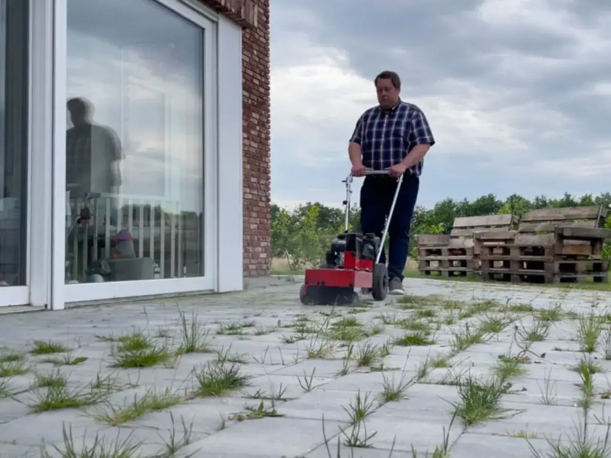 Mężczyzna zgrabnie wykonuje czyszczenie kostki brukowej z mchu i chwast&oacute;w, przywracając jej dawny blask.