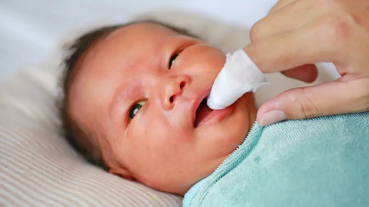 Delikatne czyszczenie dziąseł noworodka. Choć jeszcze nie widać zęb&oacute;w, troskliwa dłoń dba o higienę jamy ustnej maluszka.