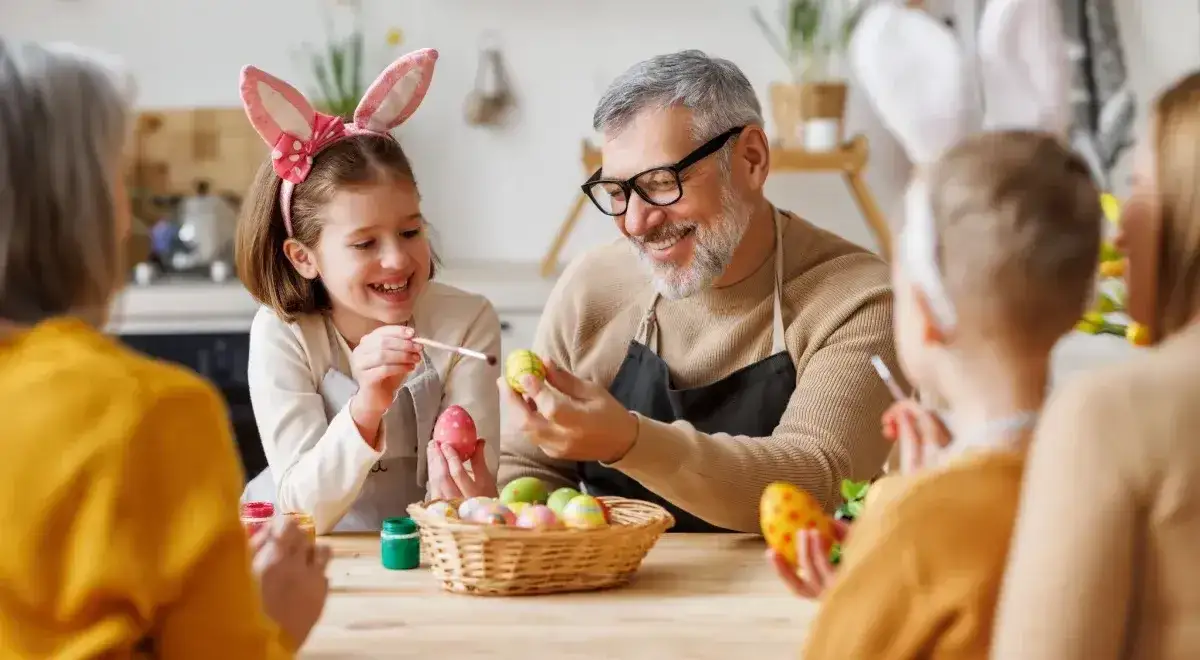 Rodzina maluje pisanki, śmiejąc się. Dzieci w kr&oacute;liczych uszach, dziadek z okularami. To rodzinne przygotowania do Wielkanocy, kt&oacute;ra jest ruchoma.