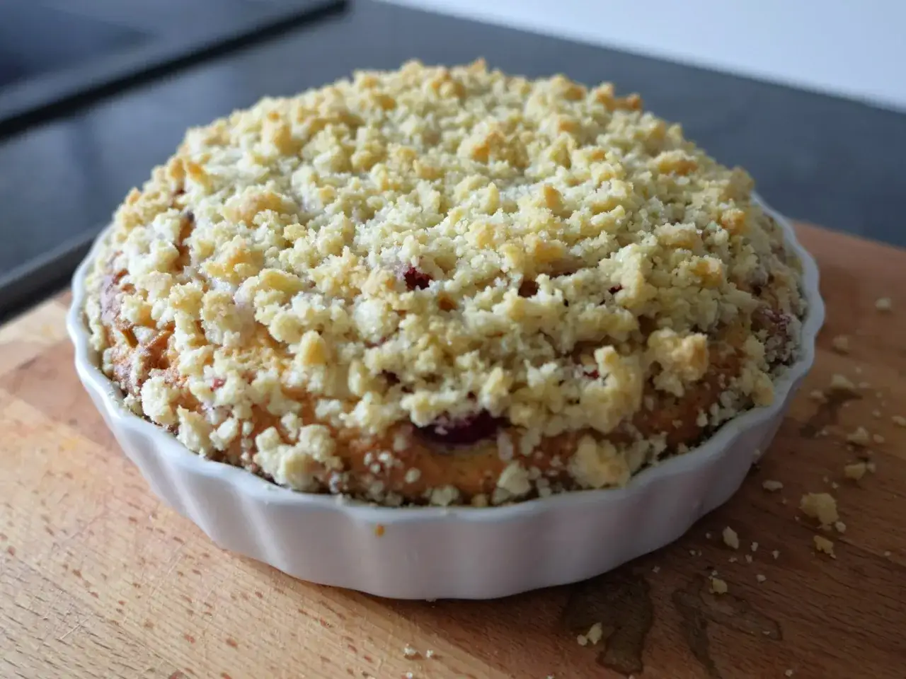 Pyszne ciasto drożdżowe bez wyrabiania Ewy Wachowicz, z kruszonką i owocami, w białej formie na drewnianej desce.