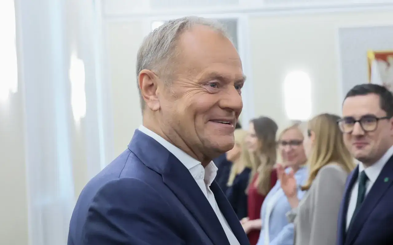 Uśmiechnięty Donald Tusk w garniturze, w tle ludzie. Wyobraź sobie, kiedy urodził się Donald Tusk, czy też tak promieniał?