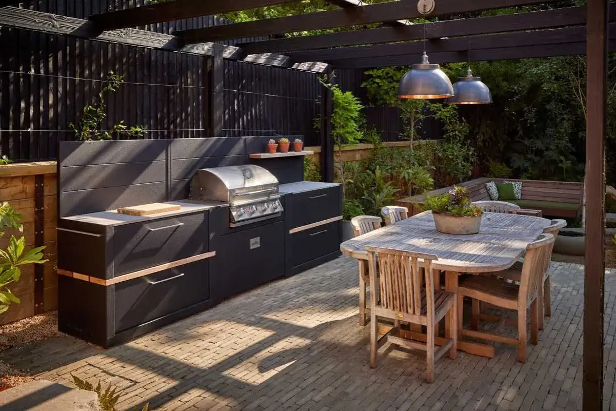 Nowoczesny grill w ogrodzie, z czarną zabudową i drewnianym stołem, zaprasza do letnich biesiad.