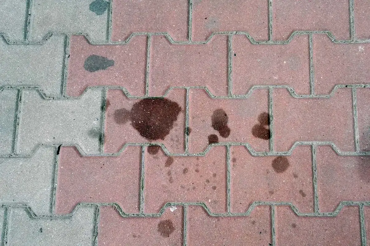 Stare plamy z oleju na kostce brukowej, świadczące o dawnych wyciekach z pojazd&oacute;w.