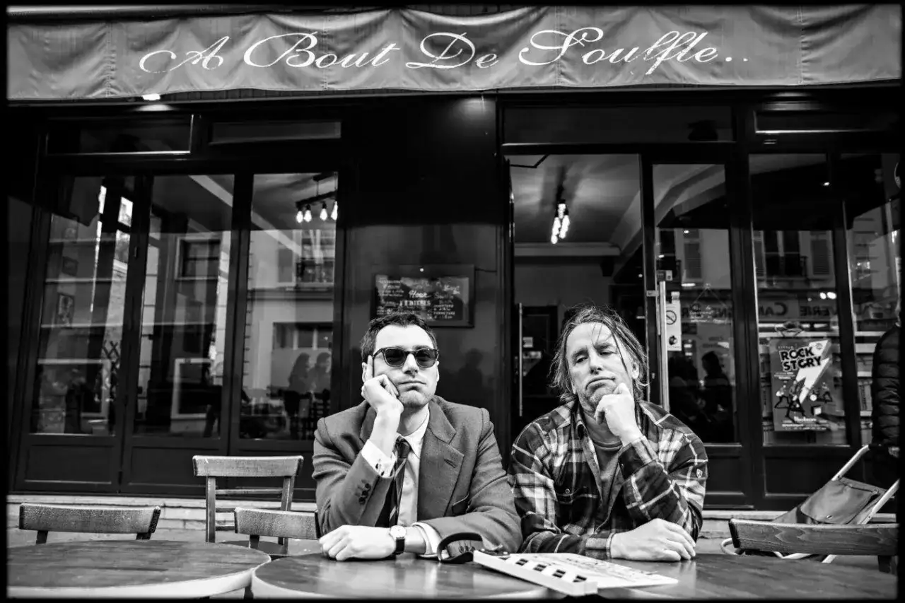 Dwóch mężczyzn siedzi przy stoliku przed kawiarnią 