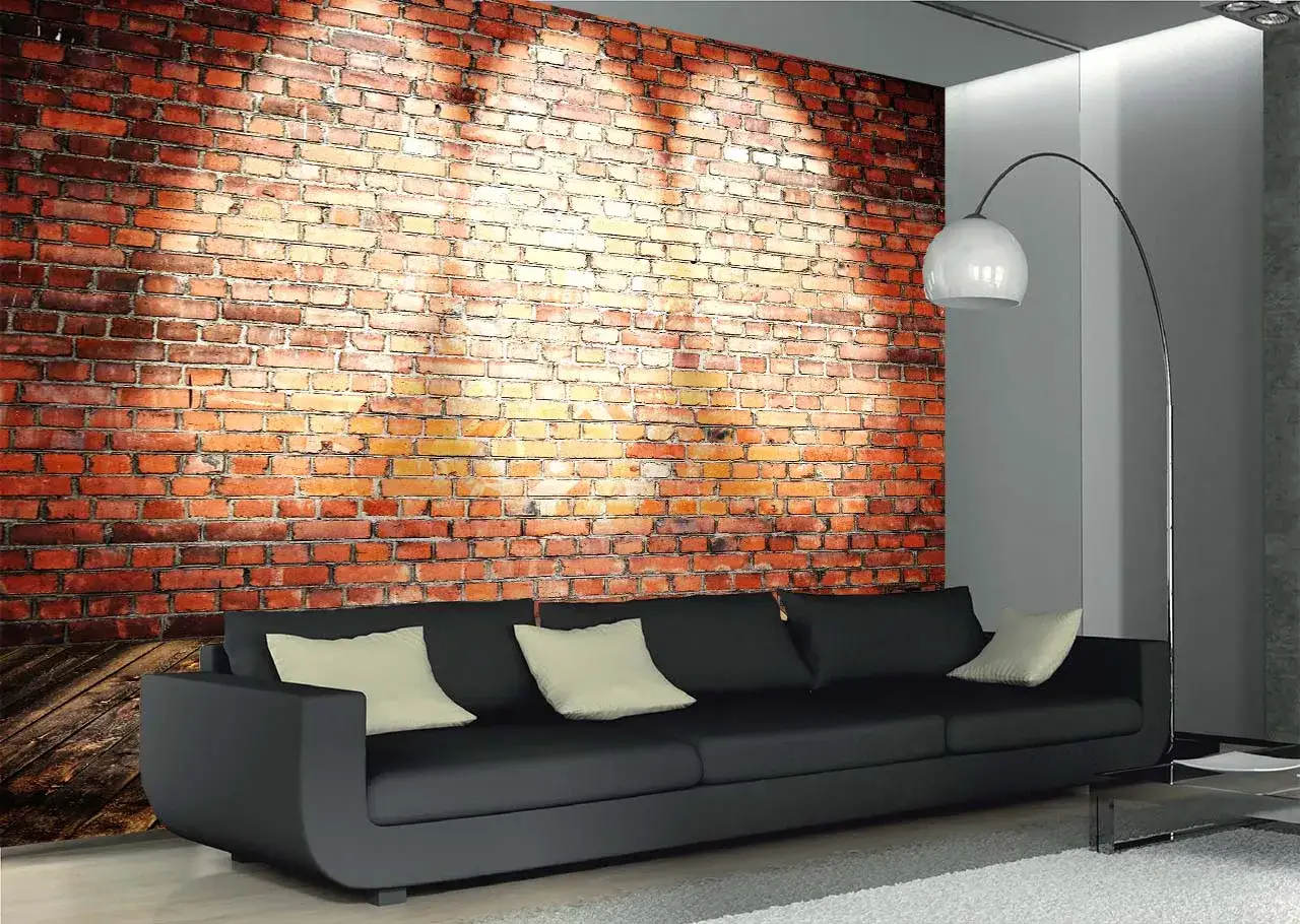 Nowoczesny salon z czarną sofą i poduszkami, na ścianie efektowna tapeta cegła czerwona z cieniem rzucanym przez lampę.