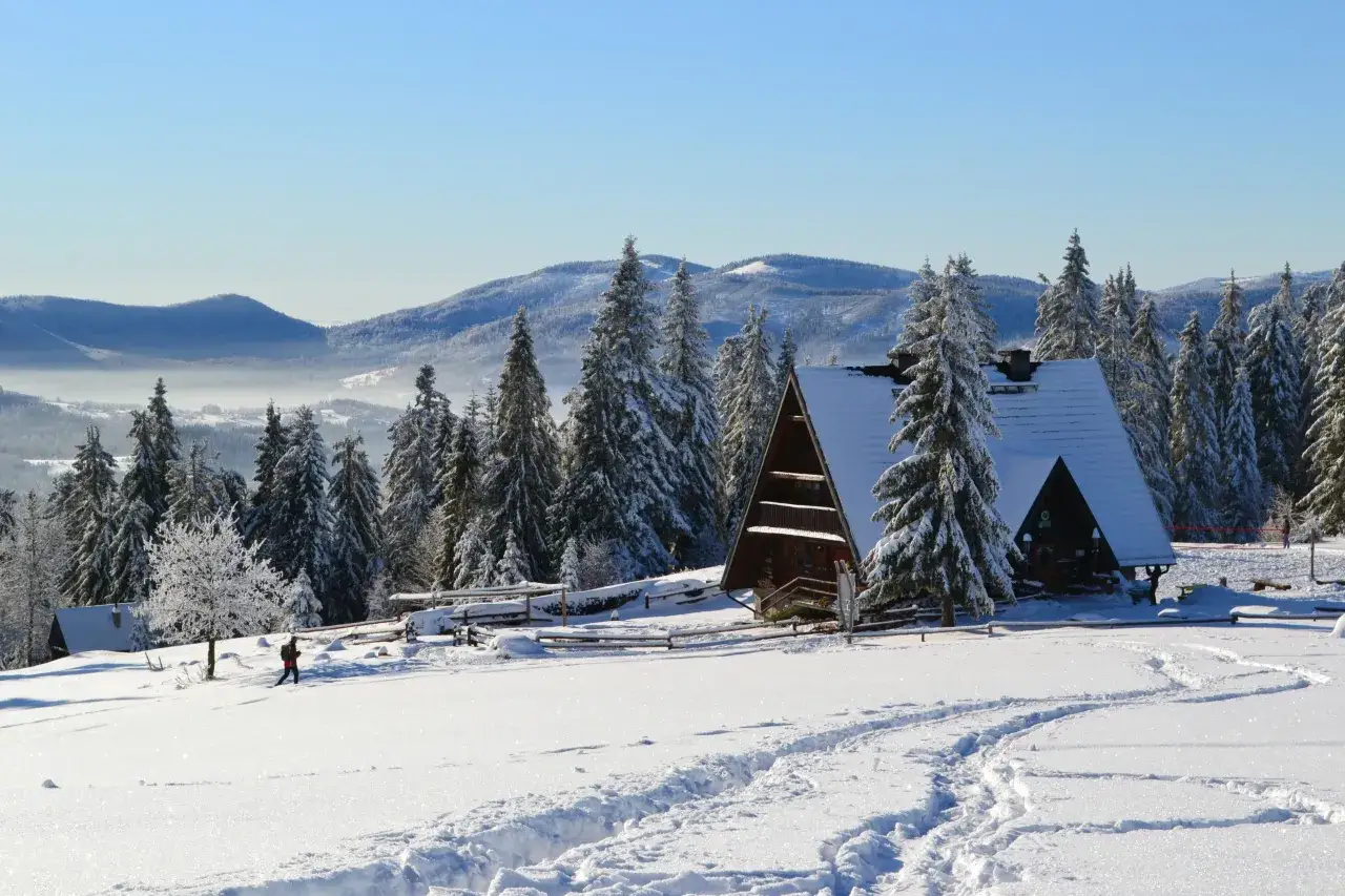 Zimowy krajobraz z bac&oacute;wką Krawc&oacute;w Wierch, ośnieżonymi drzewami i śladami na śniegu.