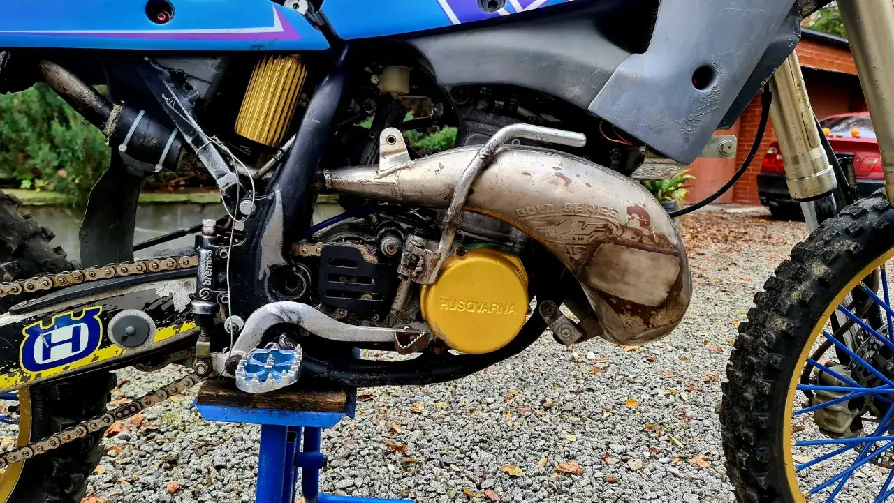 Silnik i wydech motocykla Husqvarna CR 250. Złoty filtr powietrza i ż&oacute;łta osłona silnika.