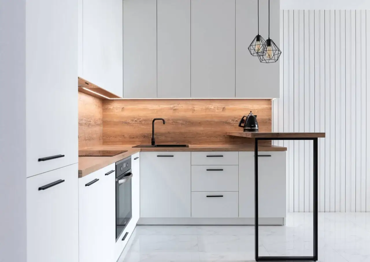 Nowoczesne białe szafki kuchenne z drewnianym panelem i czarnym blatem. Eleganckie ściany w kuchni tworzą przytulną atmosferę.