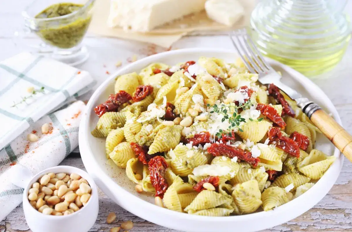 Pyszny makaron z pesto, suszonymi pomidorami i orzeszkami pinii, posypany parmezanem. Idealny na szybki obiad.