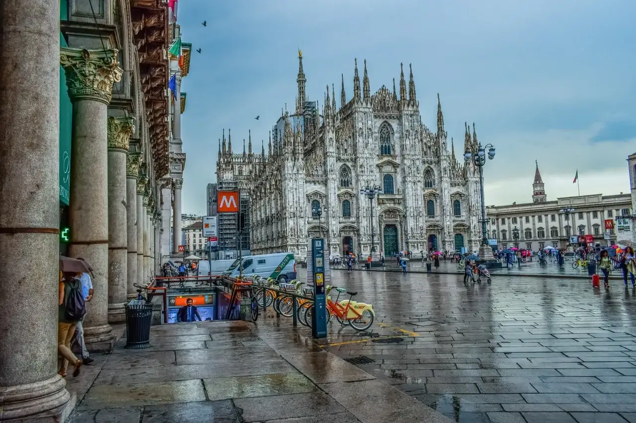 Deszczowy dzień w Mediolanie. Katedra Duomo i plac Piazza del Duomo, z ludźmi spacerującymi pod parasolami.