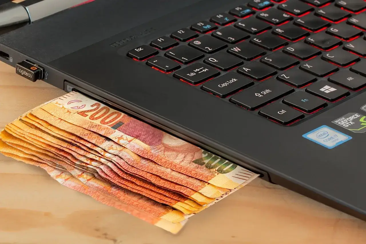 Stos banknotów wsuwa się pod laptopa z podświetlaną klawiaturą. Zastanawiasz się, ile kosztuje laptop?