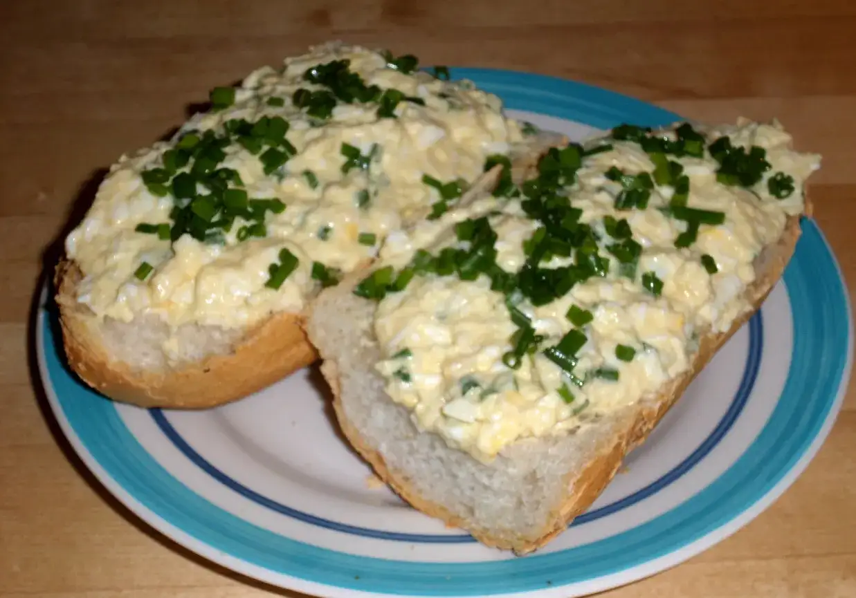 Dwie kromki chleba z obficie nałożoną pastą jajeczną z chrzanem, posypane szczypiorkiem.