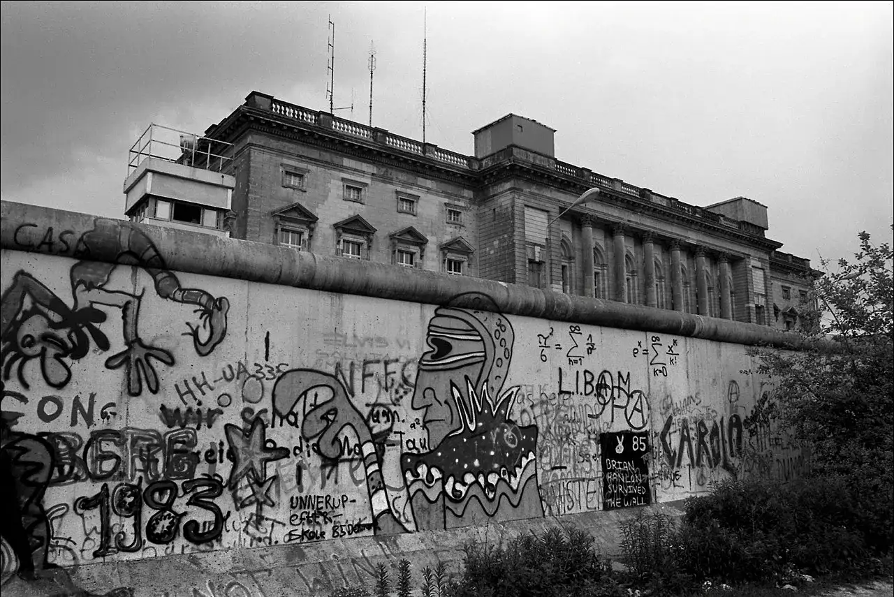 Mur Berliński pokryty graffiti, z budynkiem w tle. Widać datę 1983, kiedy wzniesiono mur berliński.