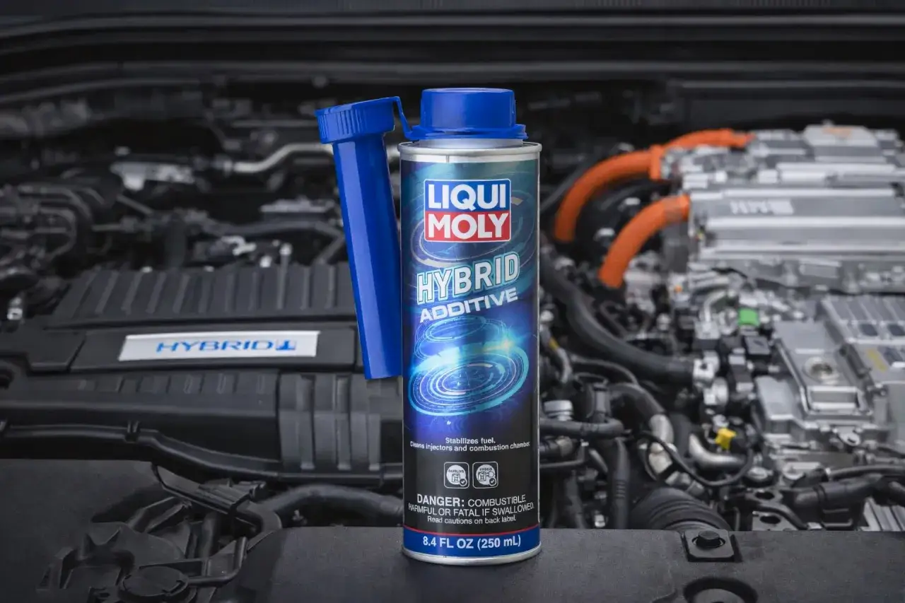 Dodatek do benzyny Liqui Moly Hybrid Additive w puszce, obok silnika hybrydowego. Dba o czystość układu paliwowego.