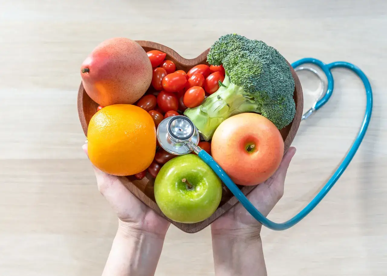 Zdrowe owoce i warzywa w kształcie serca, z niebieskim stetoskopem, symbolizujące przykładowy jadłospis przy miażdżycy.