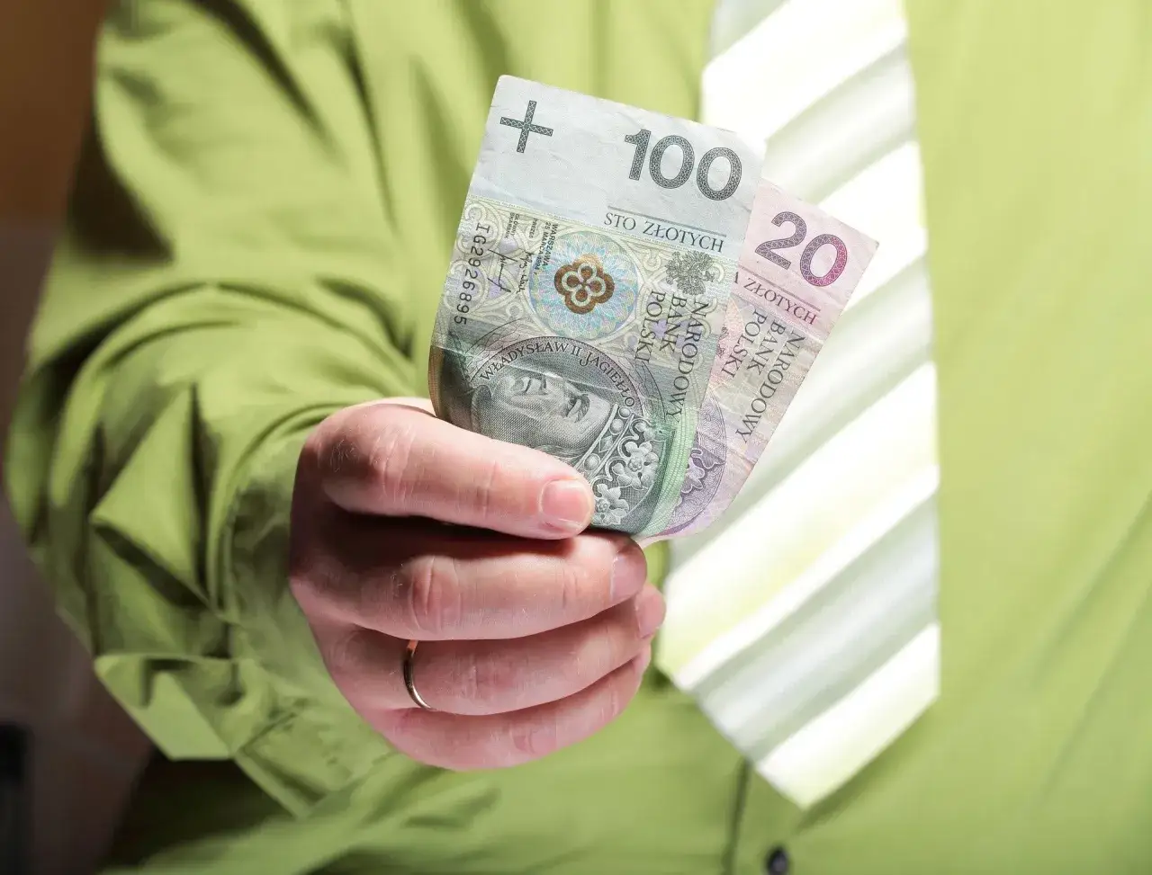 Dłoń trzyma banknoty 100 i 20 zł. Czy mieszkaniówka wlicza się do dochodu?