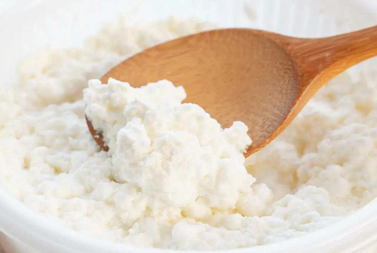 Biały ser w misce, mieszany drewnianą łyżką. Zastanawiasz się, czy można mrozić biały ser? Tak, można, choć może zmienić konsystencję.