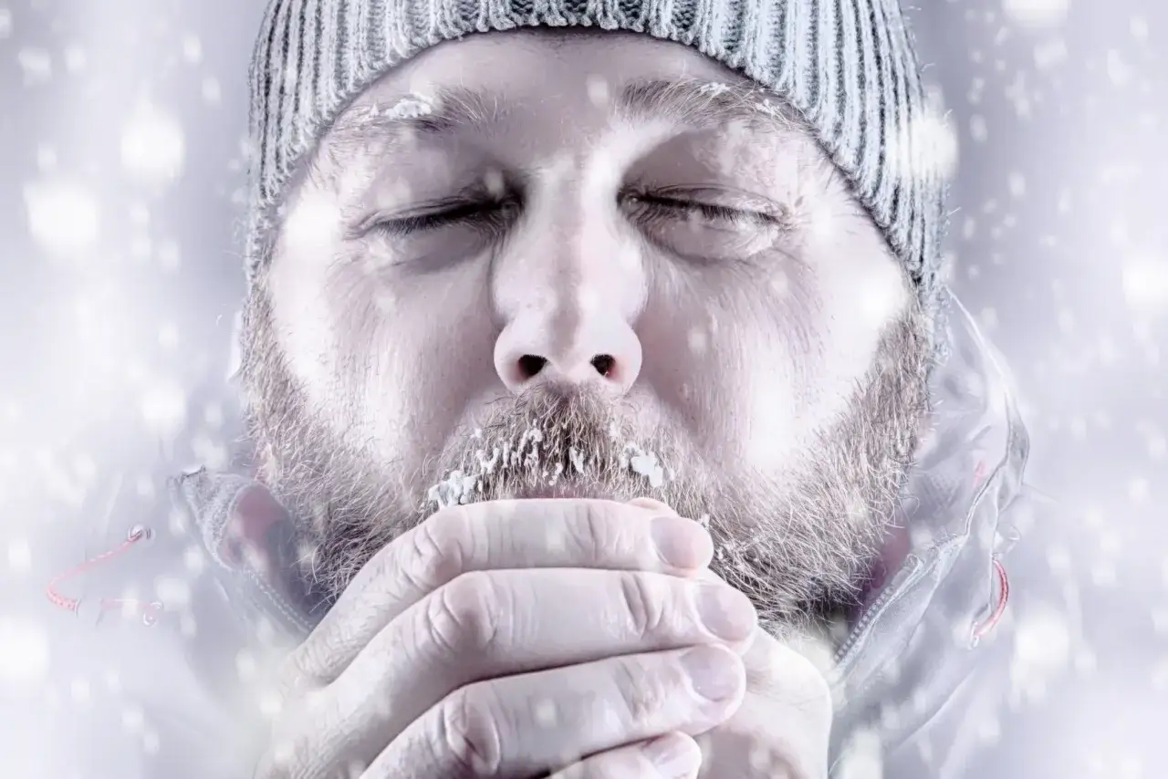 Mężczyzna z lodem na brodzie i brwiach, z zamkniętymi oczami, trzymający dłonie przy ustach. Wygląda na to, że cierpi na odmrożenie 3 stopnia.