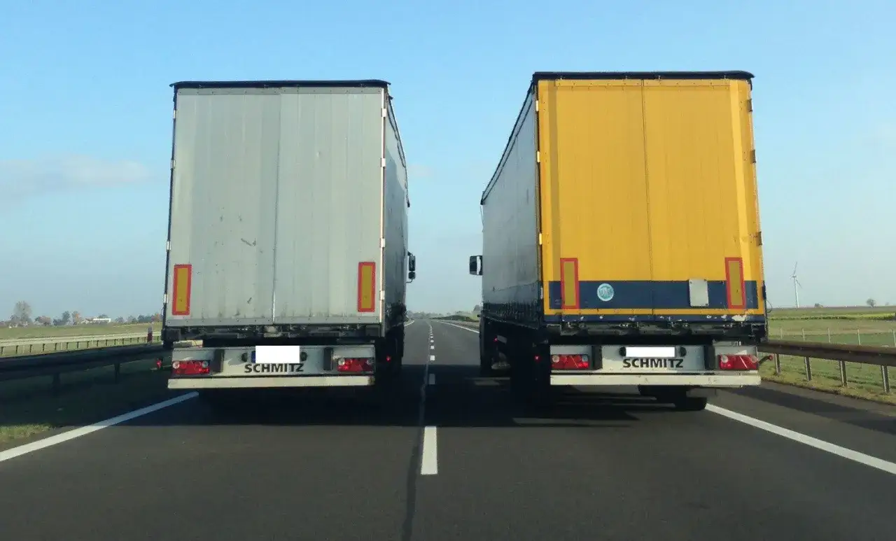 Dwie ciężarówki jadą obok siebie na autostradzie. Czy ciężarówki mogą wyprzedzać na autostradzie? To zależy od przepisów.