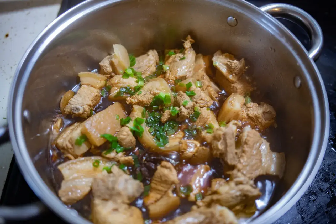 Gulasz wieprzowy w garnku, gotujący się w aromatycznym sosie, posypany szczypiorkiem. Idealny czas, by sprawdzić, ile gotować gulasz wieprzowy.