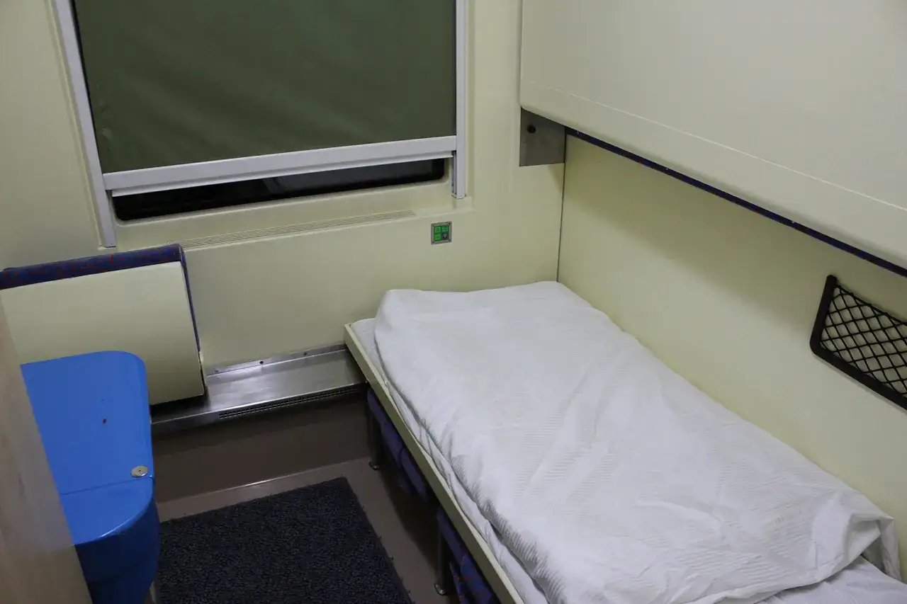 Wnętrze wagonu sypialnego Pendolino z łóżkiem, oknem i niebieskim siedzeniem.