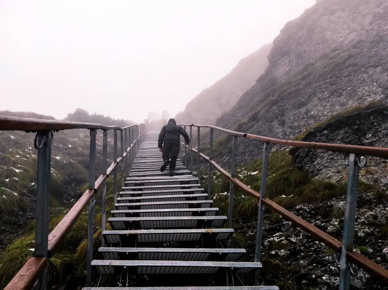 Człowiek wspina się po metalowych schodach w mglistych g&oacute;rach w Rumunii.