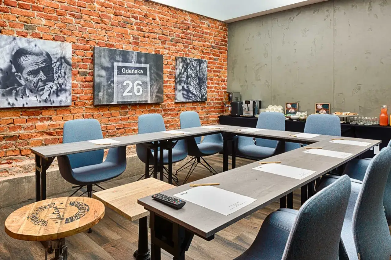 Nowoczesna sala konferencyjna w hotelu 4-gwiazdkowym, spełniająca wszelkie wymagania. Ceglana ściana, obrazy, wygodne krzesła i st&oacute;ł w kształcie podkowy.