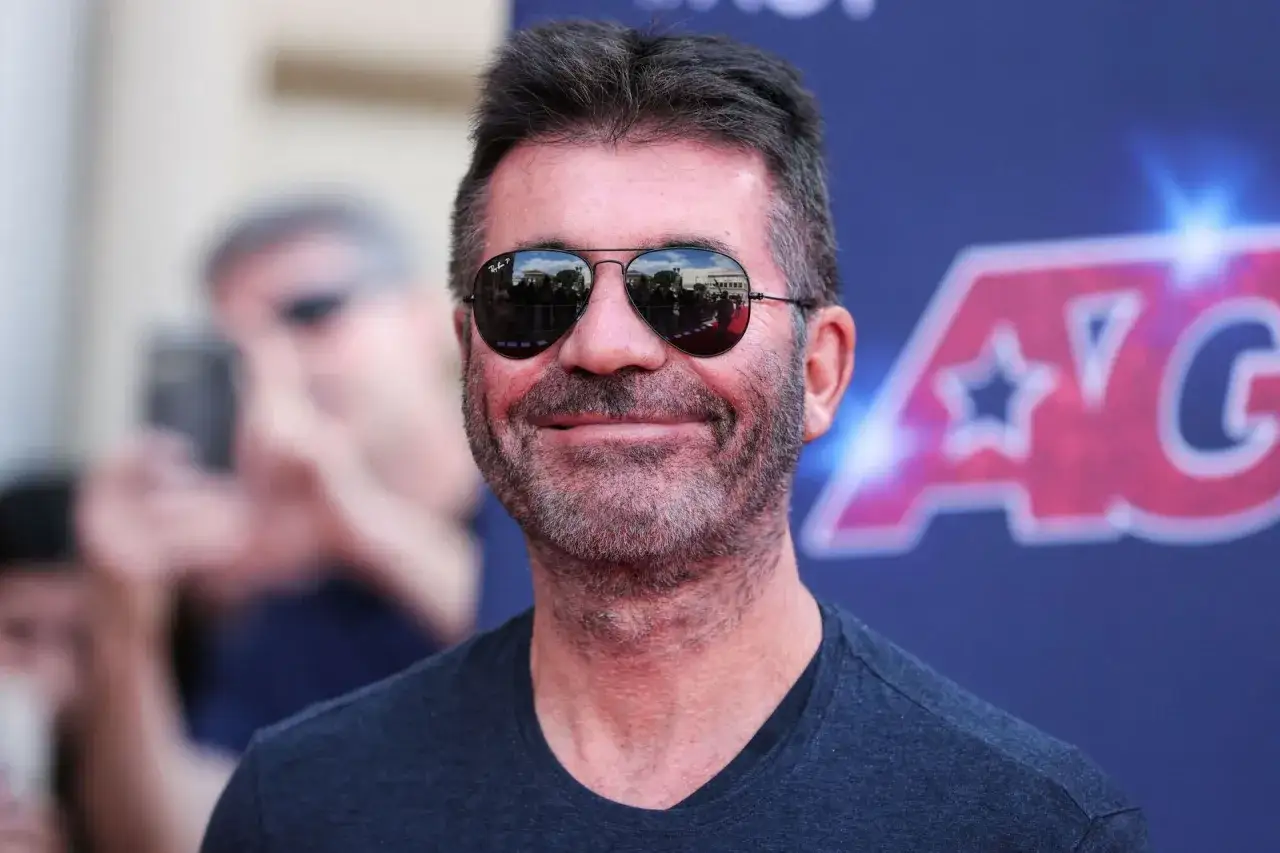 Simon Cowell w okularach przeciwsłonecznych, uśmiecha się. Plotki o tym, czy Simon Cowell nie żyje, są nieprawdziwe.