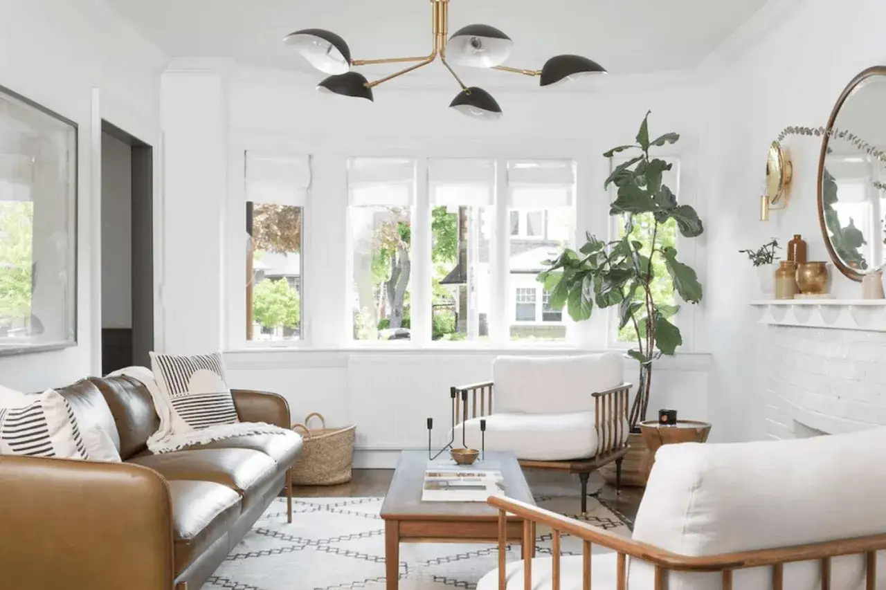 Nowoczesne punkty świetlne sufitowe w salonie z brązową kanapą, białymi fotelami i dużą rośliną.