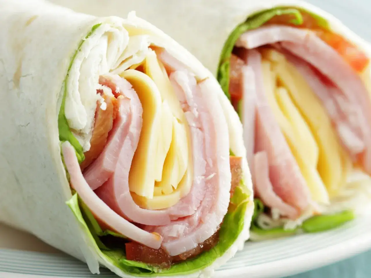 Dwa tortille zawinięte z szynką, serem i sałatą. Czy placki tortilli są zdrowe? Zależy od dodatków!