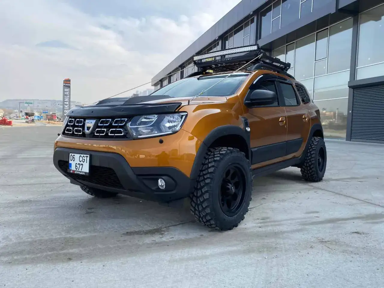 Pomarańczowy Dacia Duster off road z terenowymi oponami i bagażnikiem dachowym, gotowy na przygodę.
