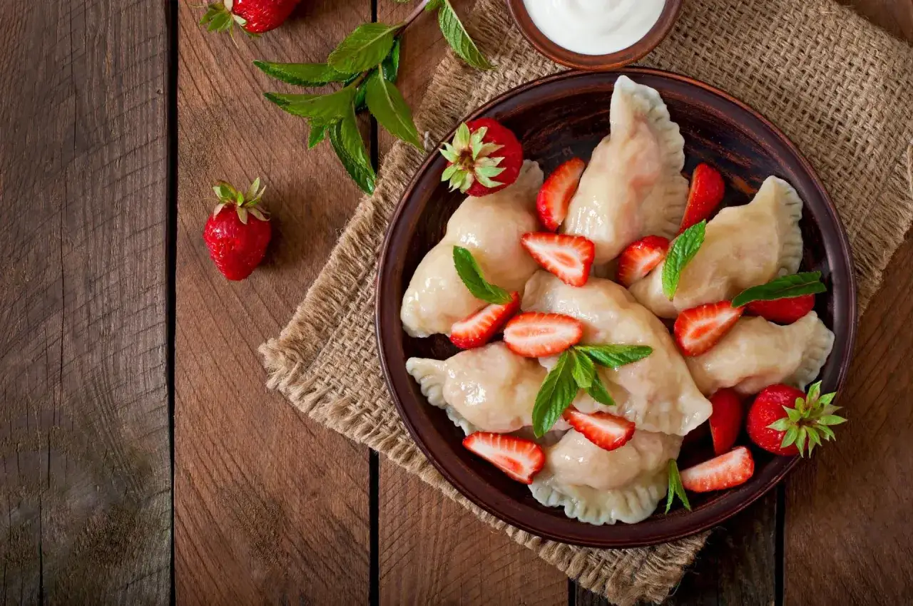 Pyszne pierogi z truskawkami, udekorowane świeżymi owocami i miętą, podane na glinianym talerzu.