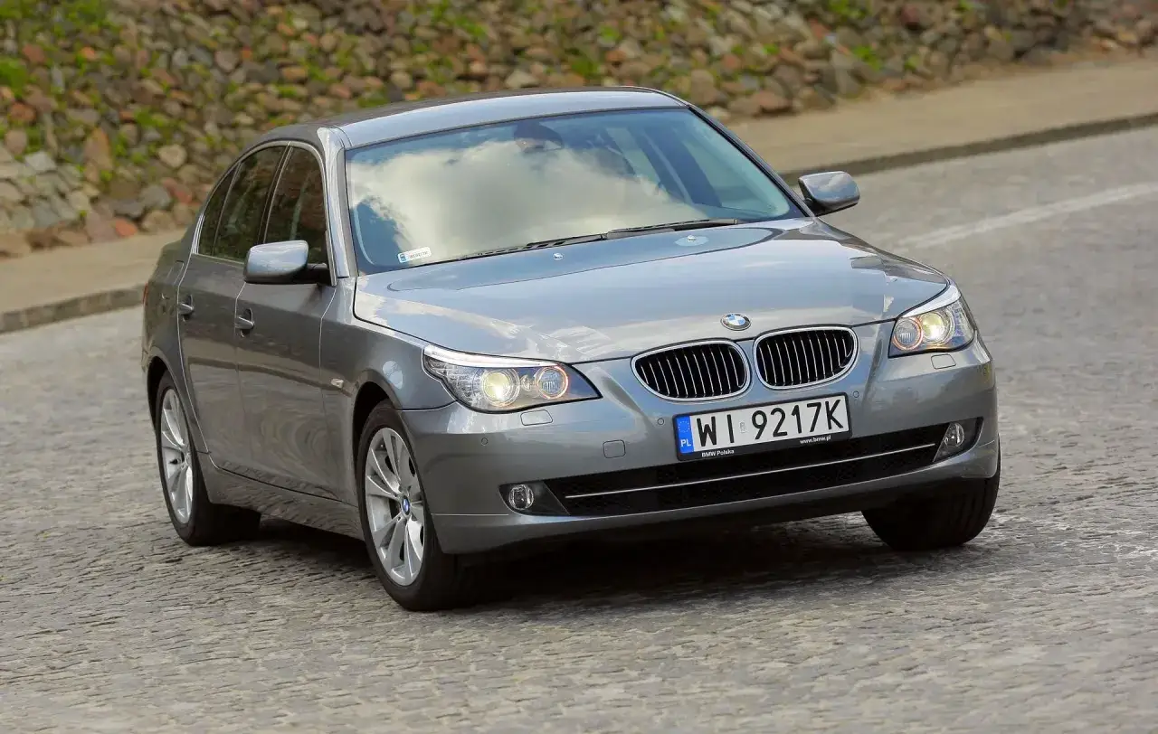 Szary sedan BMW E60 na brukowanej drodze. Kierowca zastanawia się nad spalaniem tego modelu.