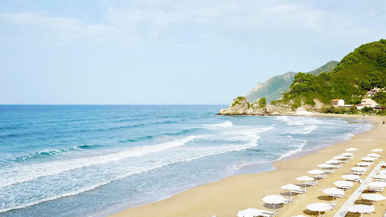 Piękna plaża z białymi parasolami, turkusowe morze i zielone wzg&oacute;rza. Czy to Korfu czy Rodos?