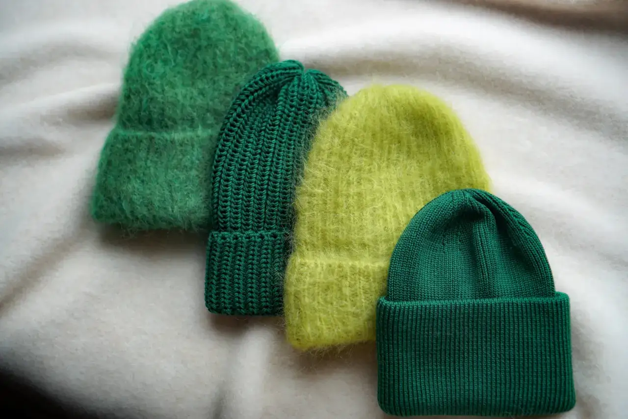 Cztery zielone czapki z merynosa, dwie puszyste, dwie prążkowane, leżą na jasnym tle.