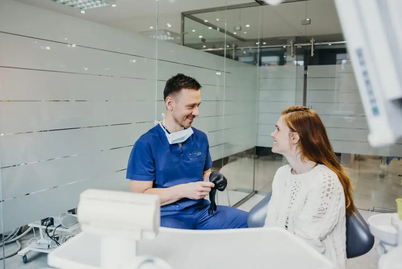 Dentysta w niebieskim uniformie rozmawia z pacjentką. Może właśnie opowiada o tym, jak pozbyć się b&oacute;lu zęba na zimne.