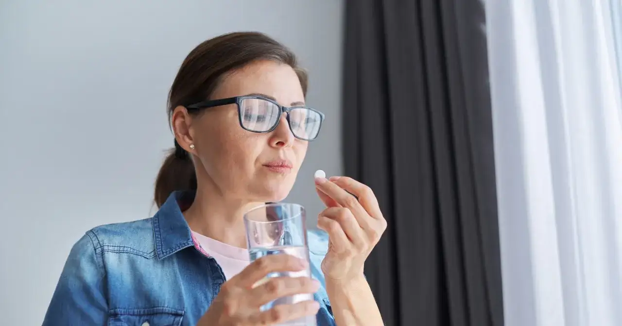 Kobieta w okularach bierze tabletkę, zastanawiając się nad mysimba skutki uboczne.