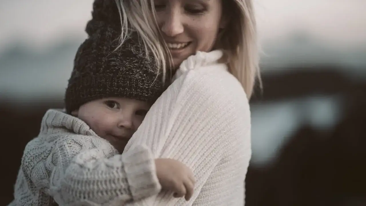 Uśmiechnięta mama tuli dziecko. Choć czasem trudno, miłość pokonuje depresję poporodową.