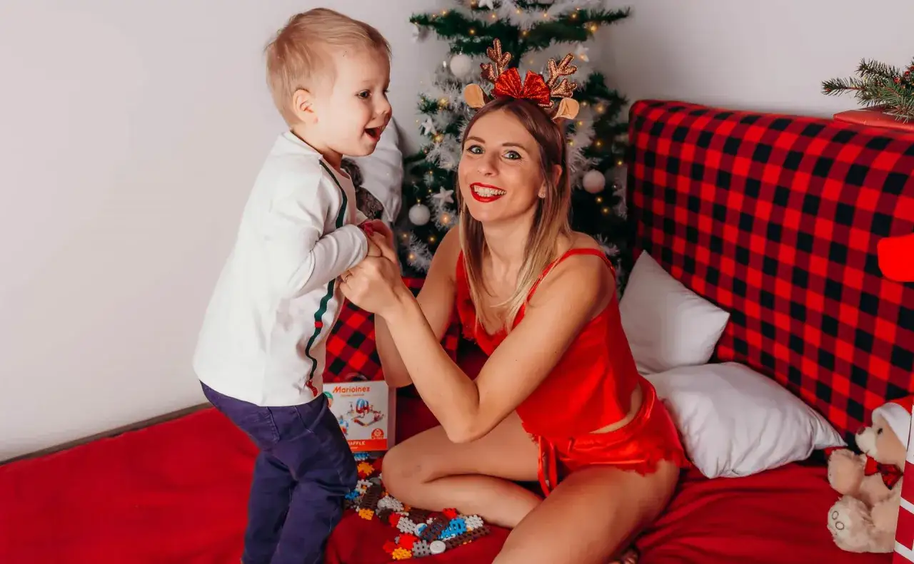 Wesoła sesja świąteczna w domu. Mama z synkiem bawią się klockami przy choince.