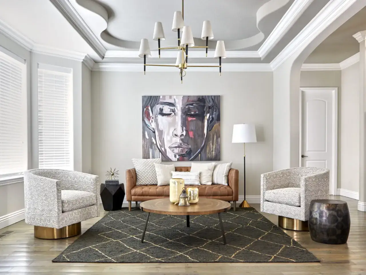 Nowoczesny salon z portretem kobiety, sk&oacute;rzaną kanapą i dwoma fotelami. Dobry design podkreśla geometryczny dywan i designerska lampa.