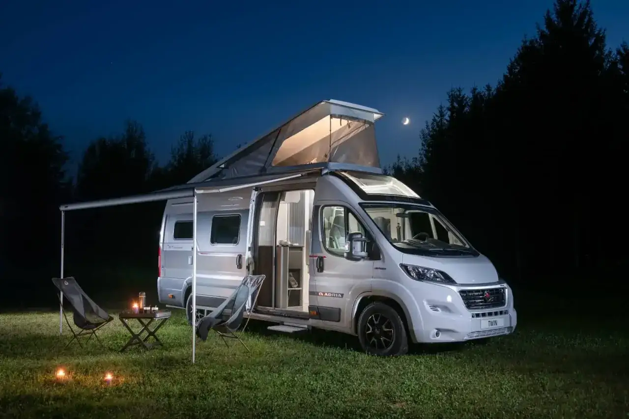 Srebrny kamper z rozłożonym namiotem dachowym i markizą, gotowy na nocleg pod księżycem. Idealny camper na wakacyjne przygody.