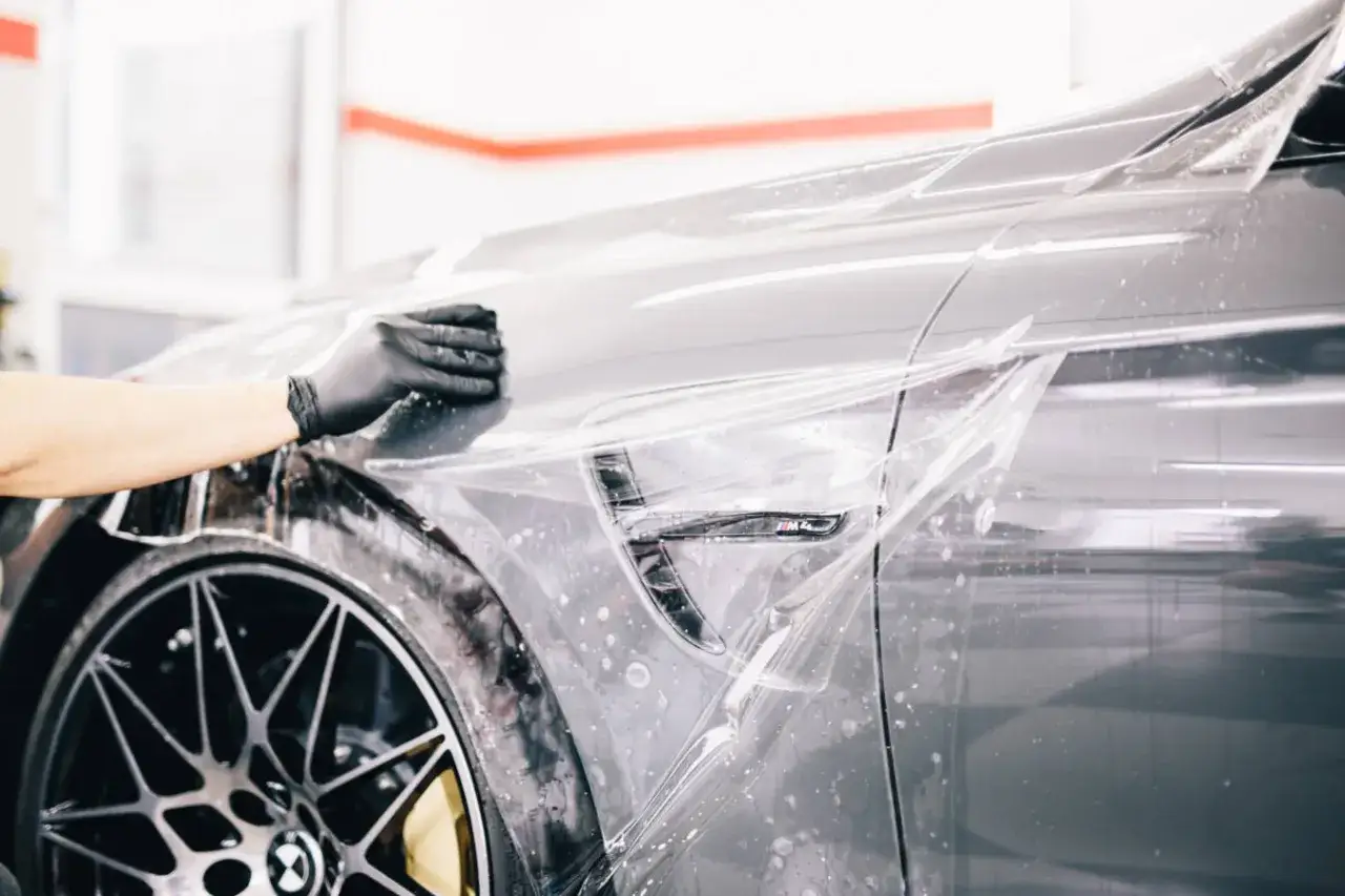 Rękawiczka w czarnej folii wygładza przezroczystą warstwę na błyszczącym lakierze samochodu. To właśnie ppf co to za ochrona!