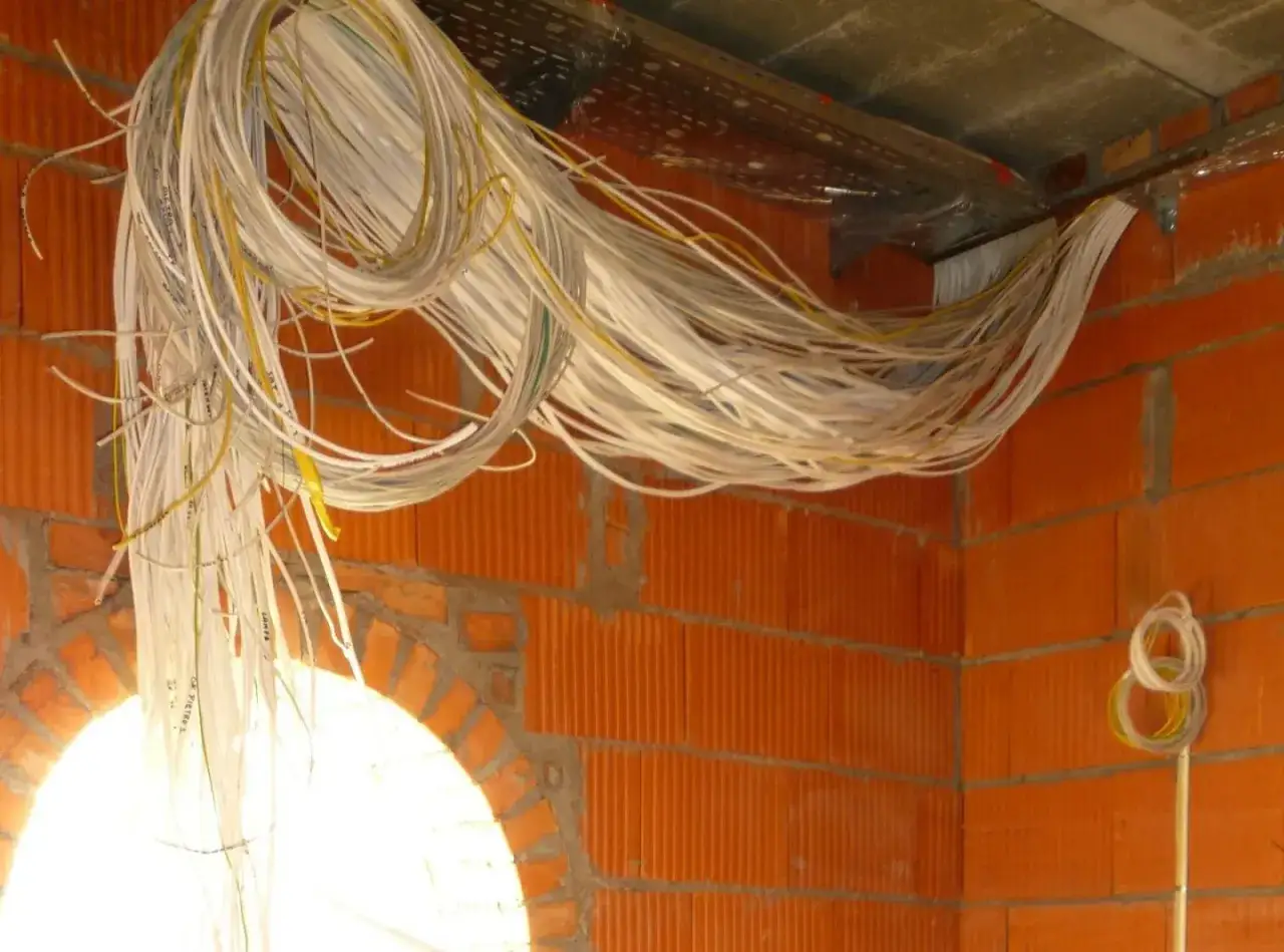Plątanina kabli, przygotowanie do instalacji system&oacute;w smart home. Pomarańczowe ściany z pustak&oacute;w, metalowe korytka.