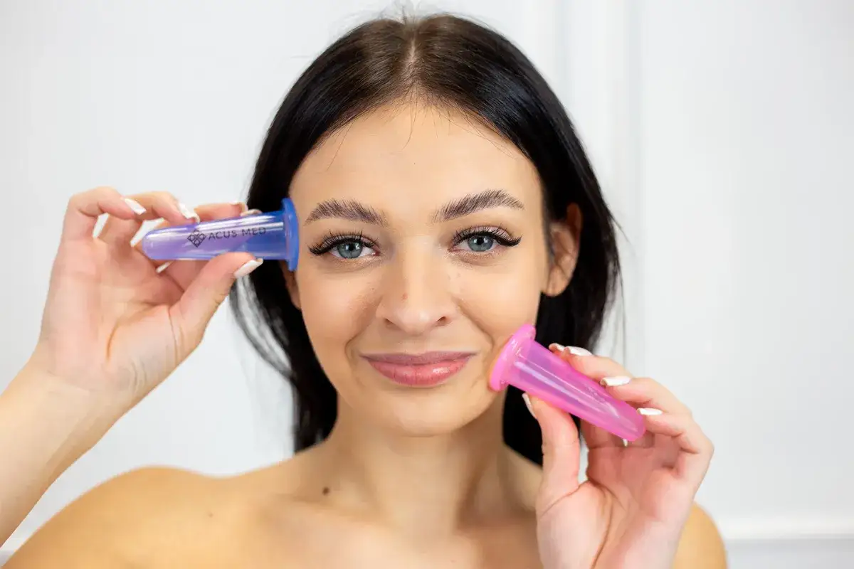 Kobieta z uśmiechem prezentuje dwie bańki chińskie do twarzy: fioletową i różową, gotowe do zabiegu.