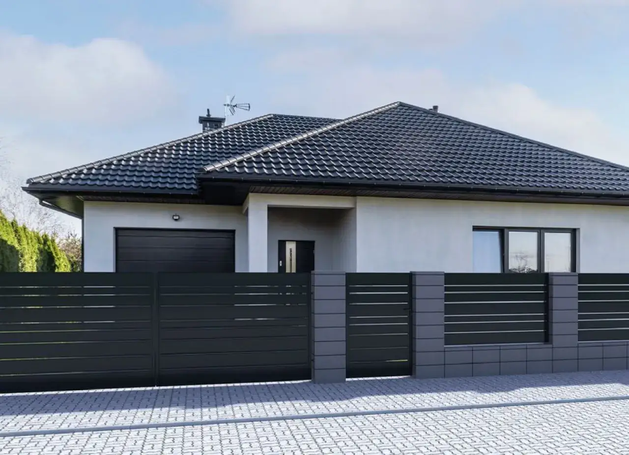 Nowoczesne ogrodzenie do ogrodu, z ciemnoszarymi panelami i betonowymi słupkami, otacza dom z garażem i dużymi oknami.