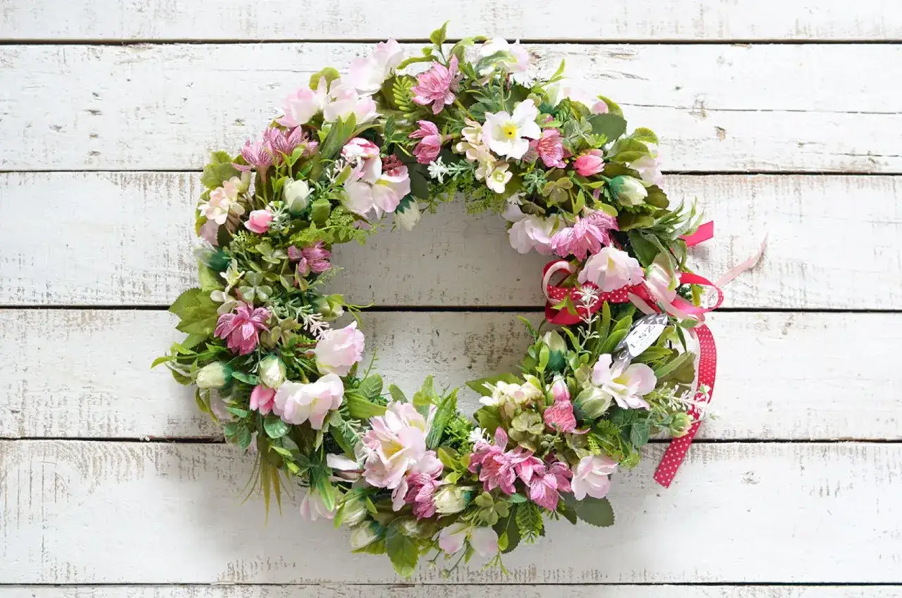 Wianek z r&oacute;żowymi i białymi kwiatami, ozdobiony wstążkami. Idealny na wielkanocne dekoracje.